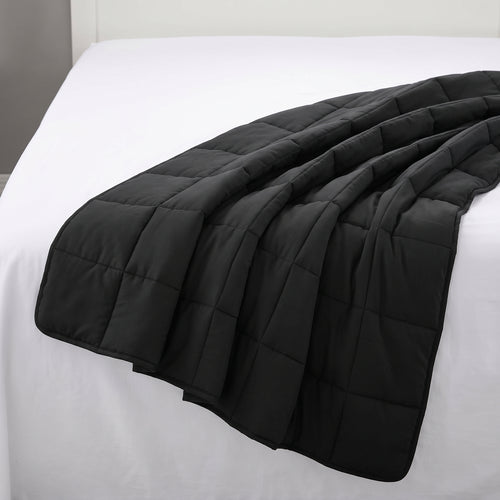 Couverture lestée Gravena carrédoux noire posée sur un lit aux draps blancs